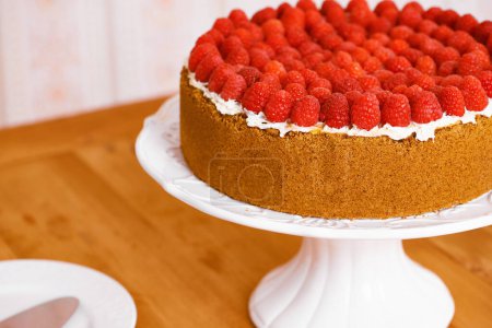 Photo for Stand, cream and cheesecake with raspberries on table for sweet snack for tea time at home. Bakery, catering and closeup of gourmet dessert with crust, frosting and fresh organic fruit in dining room. - Royalty Free Image