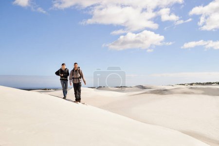 Téléchargez les photos : Couple, randonnée et sable en plein air ou désert avec dune, ciel et nuages pour la marche, l'escalade et se déplacer pour les loisirs. Homme, femme et jeune pour l'aventure dans le temps et sec pour la saison et la destination. - en image libre de droit