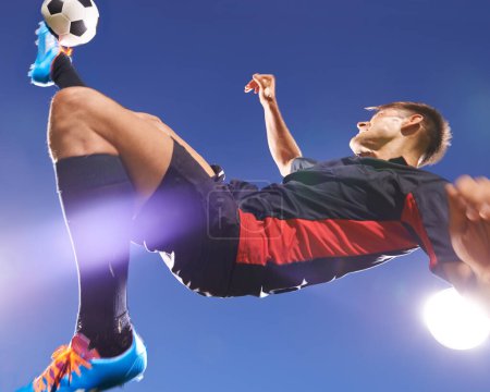 Photo for Football player, jump and kick with man and soccer ball, energy and challenge with skill in professional sport. Sky background, light and playing game at arena or stadium, action and exercise outdoor. - Royalty Free Image