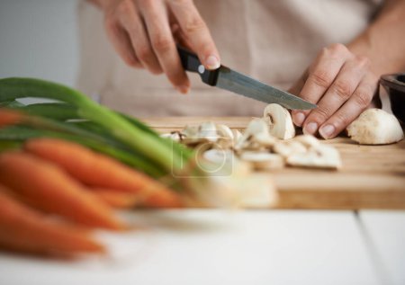 Foto de Cocina, comida y manos con verduras en cocina sobre tabla de madera para cortar, preparar comidas y nutrición. Dieta saludable, ingredientes y persona con setas para la cena vegetariana, almuerzo y ensalada. - Imagen libre de derechos