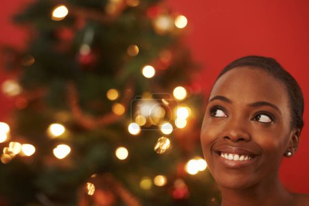 Photo for Christmas, thinking and black woman in home with tree for festive holiday and planning vacation. Happy, girl or excited for xmas in winter and ideas for house on red background in mockup space. - Royalty Free Image