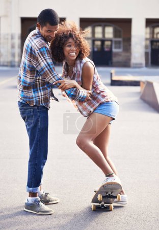 Téléchargez les photos : Heureux, l'enseignement et l'homme avec la femme sur le skateboard en ville sur romantique et amusant date ensemble. Sourire, couple et femme africaine apprenant le patinage avec un petit ami patineur dans la ville urbaine avec amour - en image libre de droit