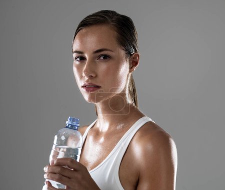 Photo for Woman, portrait and fitness with water bottle for hydration, sweat or workout on a gray studio background. Face of female person or athlete with liquid or drink for exercise in health and wellness. - Royalty Free Image