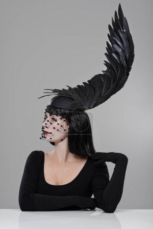 Photo for Fashion, woman and hat with feather in studio for glamour, style and thinking with mystery. Female person, confidence and cap with wing for elegance, luxury and designer clothes on gray background. - Royalty Free Image