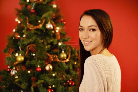 Photo for Happy woman, portrait and celebration by christmas tree on red background and indoor for winter holiday. Young, person or smile on face for xmas season for present or natural pine with decoration. - Royalty Free Image