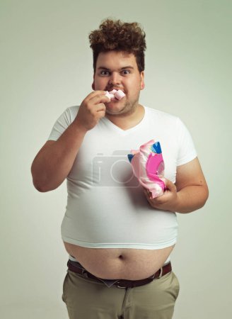 Photo for Portrait, hunger and marshmallow with plus size man in studio on gray background for unhealthy eating. Food, hungry for sweets and candy with young person with snack bag or packet for greed or belly. - Royalty Free Image