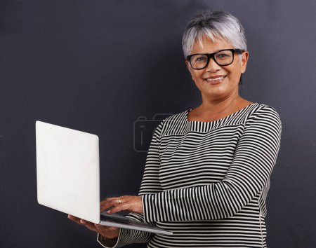 Photo for Laptop, typing and portrait of mature woman in studio background learning about technology or website. Senior, person and education on computer for communication, connection and social networking. - Royalty Free Image