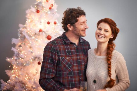 Photo for Love, smile and wine with couple at Christmas to decorate to tree in studio on gray background. Alcohol, celebration or festive portrait with happy man and woman together for December holiday season. - Royalty Free Image