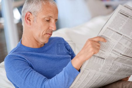 Photo for Senior, man and reading a newspaper on sofa for article, information and morning routine in living room of home. Elderly, person and media paper for global news, knowledge or relax on couch in lounge. - Royalty Free Image