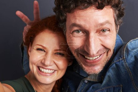 Photo for Couple, face and happy in selfie, playful for social media with bunny ears or peace sign on blue background. Portrait, fun in picture and photography, people and smile with energy and silly together. - Royalty Free Image