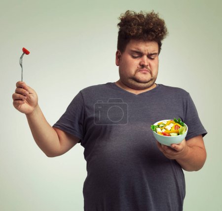 Photo for Studio, unhappy man and salad with bowl for healthy meal, diet and nutrition for weight loss. Plus size, male person and disgust expression with organic food for wellness, detox or lifestyle change. - Royalty Free Image