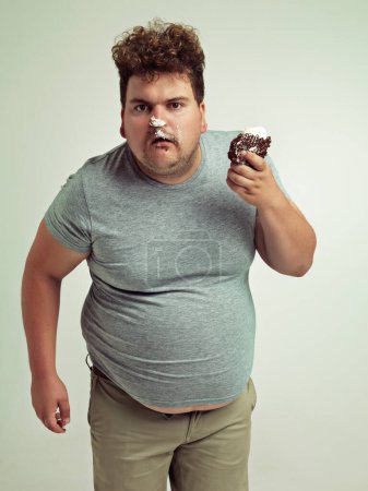 Photo for Plus size, eating and portrait of man with cake in studio for unhealthy, sugar and sweet snack. Greedy, food and male person with messy slice of chocolate dessert isolated by gray background - Royalty Free Image