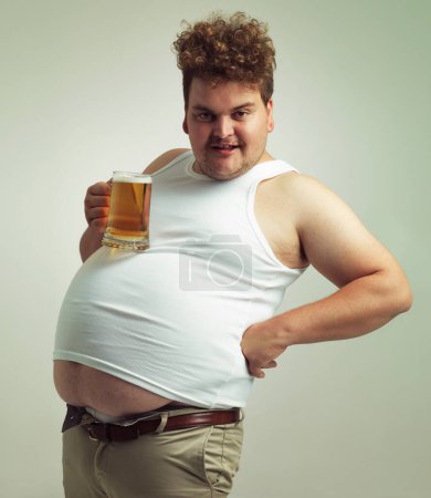 Photo for Obese, weight gain and lager for man in studio with drink for unhealthy habit, plus size and joke. Overweight person with glass on fat stomach for balance, drunk and humor for alcohol and comic. - Royalty Free Image
