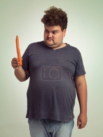 Photo for Man, vegetables and carrot in studio with thinking for healthy snack, detox and vitamin c for wellness. Plus size, male person and unhappy with organic food for nutrition, lifestyle and diet. - Royalty Free Image