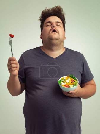 Photo for Plus size man, salad and diet with healthy food with fork, bowl and vegetables for wellness on studio background. Male person, frustrated and lose weight for health, eating disorder and nutrition. - Royalty Free Image