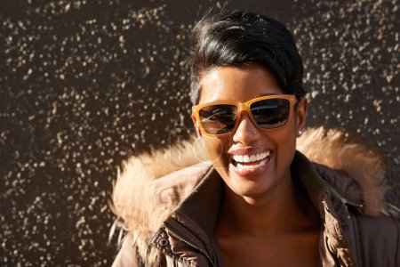 Photo for Woman, sunglasses and smile with portrait, sunshine and accessorise for trendy fashion. Model, laugh and jacket with style, happiness and urban outdoor background with grey wall and cool sunrise. - Royalty Free Image