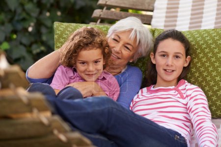 Photo for Senior woman, grandchildren and hammock in garden with smile to relax for retirement, break and enjoy. Portrait, girls and happy in home in summer or hot weather for school holiday with grandma. - Royalty Free Image