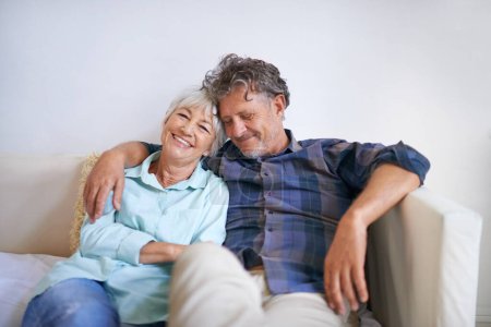 Photo for Old couple, hug and relax on sofa with happiness at home, love and security with comfort for bonding. Marriage, partner and retirement together with smile, trust and loyalty with people in lounge. - Royalty Free Image