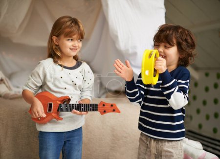 Foto de Música, juego y niños con instrumentos en el dormitorio para la diversión, vinculación y práctica de la banda. Feliz, sonrisa y niña y niños con juguetes de guitarra y pandereta disfrutando de la canción musical en casa - Imagen libre de derechos
