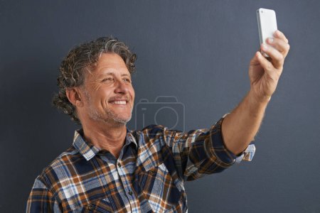 Photo for Mature, man and happy selfie in studio and learning about photography on dark background. Filming, video or click record for profile picture and post online to social media with website or blog. - Royalty Free Image