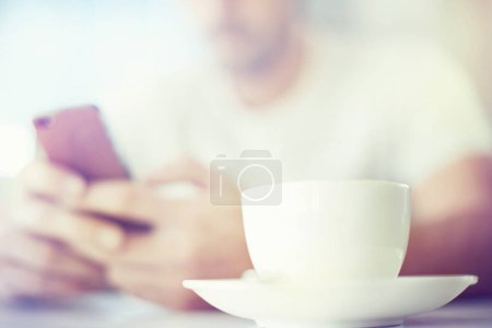 Foto de Hombre, manos y taza de té con teléfono en la cafetería para la comunicación, la mañana o las redes sociales. Primer plano de la persona masculina con bebida o bebida en el teléfono inteligente móvil para chatear en línea o mensajes de texto en la cafetería. - Imagen libre de derechos