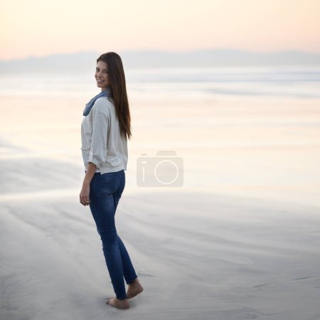 Téléchargez les photos : Femme, marche et heureux en portrait par l'océan, coucher de soleil et vacances avec la nature pour se détendre à la plage. Fille, personne et en plein air par la mer avec les pieds dans le sable pour des vacances, aventure ou sourire par la mer en Australie. - en image libre de droit