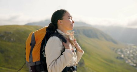 Photo for Young woman, trekking on mountains and breathing fresh air for outdoor wellness, fitness and health. Happy person in wind with backpack and hiking in nature on a hill for adventure, travel or journey. - Royalty Free Image