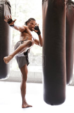 Téléchargez les photos : Homme, kick boxing et sac avec entraînement, pied et combat pour l'exercice avec équilibre, puissance et précision dans la salle de gym. Athlète, personne ou combattant africain avec entraînement, remise en forme ou frappe pour le défi dans le dojo. - en image libre de droit