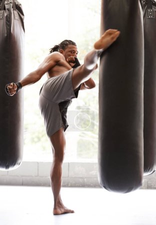Foto de Hombre, kick boxing y bolsa con ejercicio, pie y combate para entrenar con equilibrio, potencia y precisión en el gimnasio. Atleta africano, persona o luchador con entrenamiento, fitness o strike para desafío en dojo. - Imagen libre de derechos