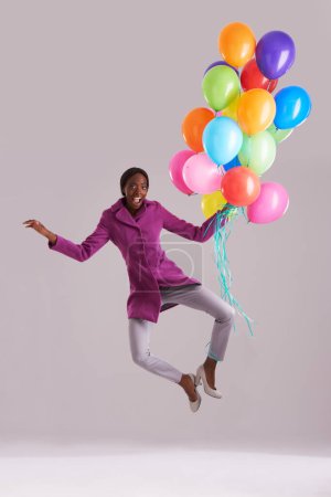 Téléchargez les photos : Ballon, saut et portrait de femme noire heureuse en studio pour l'anniversaire, la célébration et le cadeau. Mode, personne excitée et isolée avec gonflable pour la partie, cadeau et surprise sur fond gris. - en image libre de droit