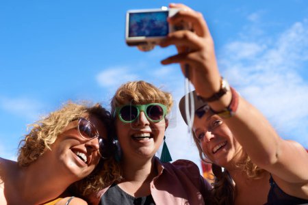 Téléchargez les photos : Amis, groupe et selfie en plein air pour festival, photographie et appareil photo numérique pour portrait. Musique, gens et ciel bleu en été, ensemble et heureux avec la culture de la musique dans le carnaval et sourire. - en image libre de droit