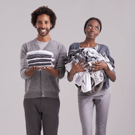 Photo for Young, couple and laundry or clothes for helping, support and thinking of house, task or home management in studio. African man and woman with domestic ideas for gender equality on a gray background. - Royalty Free Image