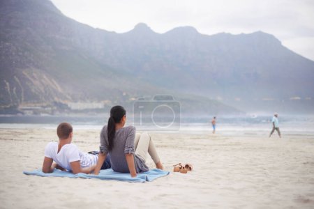 Photo for Couple, beach and vacation on blanket, picnic or relaxing on seashore by mountains. Romantic, honeymoon and love between happy husband and wife, married and date on ocean coast enjoying sunshine. - Royalty Free Image