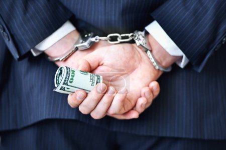 Photo for Business person, hands and money with handcuffs for bribe, secret or corruption in financial crime. Closeup or rear view of employee with roll of cash, paper or laundering finance in bribery or fraud. - Royalty Free Image