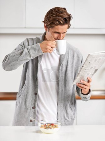 Photo for Coffee, breakfast and man with newspaper in kitchen for information at modern apartment. Nutrition, cereal and young male person drinking cappuccino or latte and reading journalism article at home - Royalty Free Image