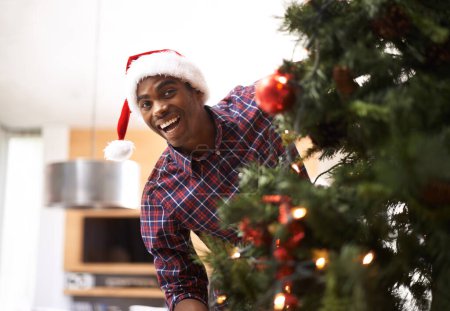Photo for Portrait, energy and black man with Christmas tree in living room of home for decoration or holiday. Smile, celebration in December and happy young person in apartment with Santa hat for tradition. - Royalty Free Image