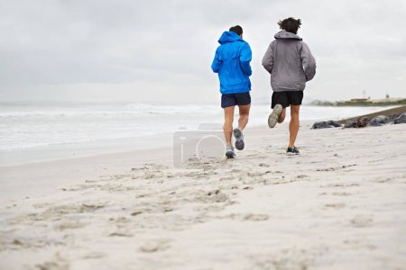 Photo for Rear view, men and running on beach, sand and fitness for wellness and gym wear in cold coast. Male athletes, jog and training for seaside, health and outdoor for sport and exercise together. - Royalty Free Image