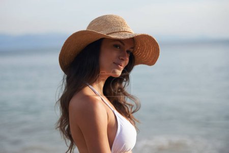 Téléchargez les photos : Sourire, vacances et femme avec chapeau à la plage pour voyager aventure, penser et se détendre dans la nature. Soleil, été et visage heureux de la fille à l'océan en vacances avec de l'eau, réflexion et station balnéaire à Bali - en image libre de droit