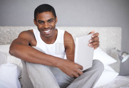 Foto de Hombre negro, retrato y cama con tablet para redes sociales, comunicación o entretenimiento en línea en casa. Hombre africano con sonrisa para la tecnología, la creación de redes o navegar en el dormitorio de la casa. - Imagen libre de derechos