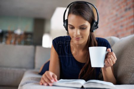 Photo for Book, coffee and music with woman on sofa in living room of home, reading to relax at weekend. Storytelling, headphones and drinking tea with young person in apartment for hobby, leisure or time off. - Royalty Free Image