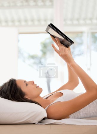 Photo for Woman, ebook and tablet on bed reading, girl and device for online entertainment from home. Browsing and social media communication while relaxing, female person and scrolling for literature novel. - Royalty Free Image