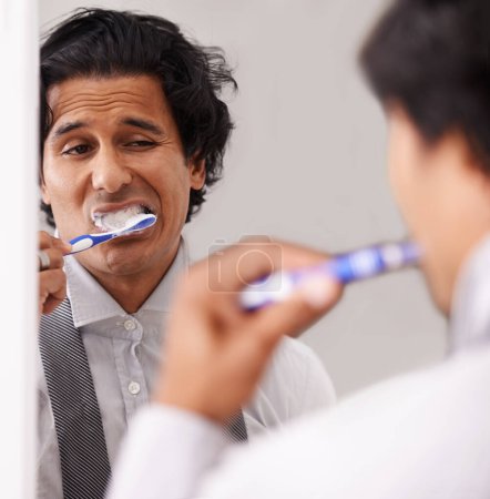 Businessman, face and brushing teeth in mirror for morning routine, hygiene or cleanliness at home. Closeup of young man or employee in tooth whitening or cleaning mouth, gum or oral for dental care.