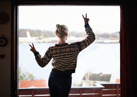 Peace sign, view and woman at window with lake, emoji and relaxed on holiday and vacation. Back, travel and female person on getaway, leisure and symbol on trip, retreat and acomodation for trip.