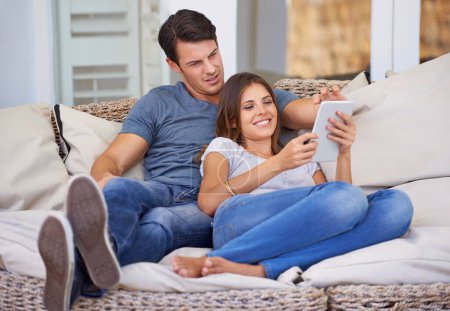 Téléchargez les photos : Couple heureux, détendez-vous et canapé avec tablette pour le cinéma, les médias sociaux ou le divertissement ensemble à la maison. Homme et femme couchés avec le sourire sur la technologie pour le streaming en ligne, série ou spectacle dans le salon. - en image libre de droit