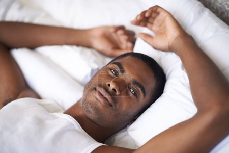 Photo for Black man, portrait and morning with bed in relax for wakeup, comfort or resting on duvet or sheets at home. Face of African male person lying awake in bedroom with pajamas for weekend at the house. - Royalty Free Image
