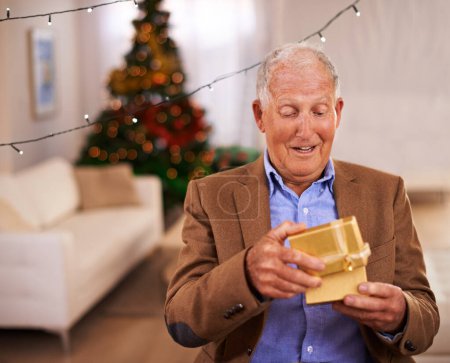 Photo for Christmas, surprise and old man with gift, home and excited with happiness and cheerful in a living room. Pensioner, apartment and elderly guy with present and party with box and retirement with wow. - Royalty Free Image