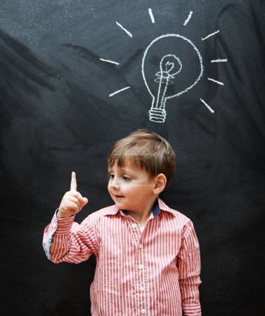 Photo for Child, solution and lightbulb on chalkboard for ideas, learning and education in school with answer or questions. Happy kid, student or boy with light bulb, emoji and creative knowledge on blackboard. - Royalty Free Image