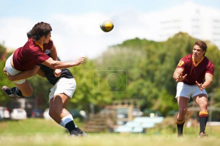 Photo for Working together for stronger unity. Shot of a young rugby player executing a pass mid-tackle - Royalty Free Image