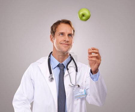 Photo for Man, doctor and apple for healthcare in studio, medical expert and dietician on gray background. Male person, fruit and proud of choice or decision for nutrition, vitamins and minerals for health. - Royalty Free Image