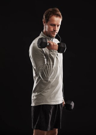 Photo for Man, dumbbells and weightlifting exercise in studio or fitness performance, training or black background. Male person, equipment and earphones for music playlist or healthy, streaming or mockup space. - Royalty Free Image